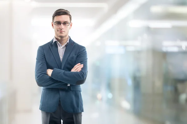 Молодой красивый бизнесмен в очках в офисе и стоя только руки перешли — стоковое фото